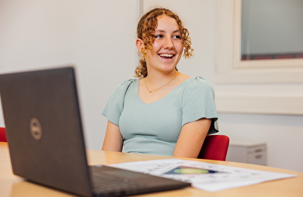 Meisje met krullende haren in een staart en een blauw shirt lacht naar de jeugdverpleegkundige